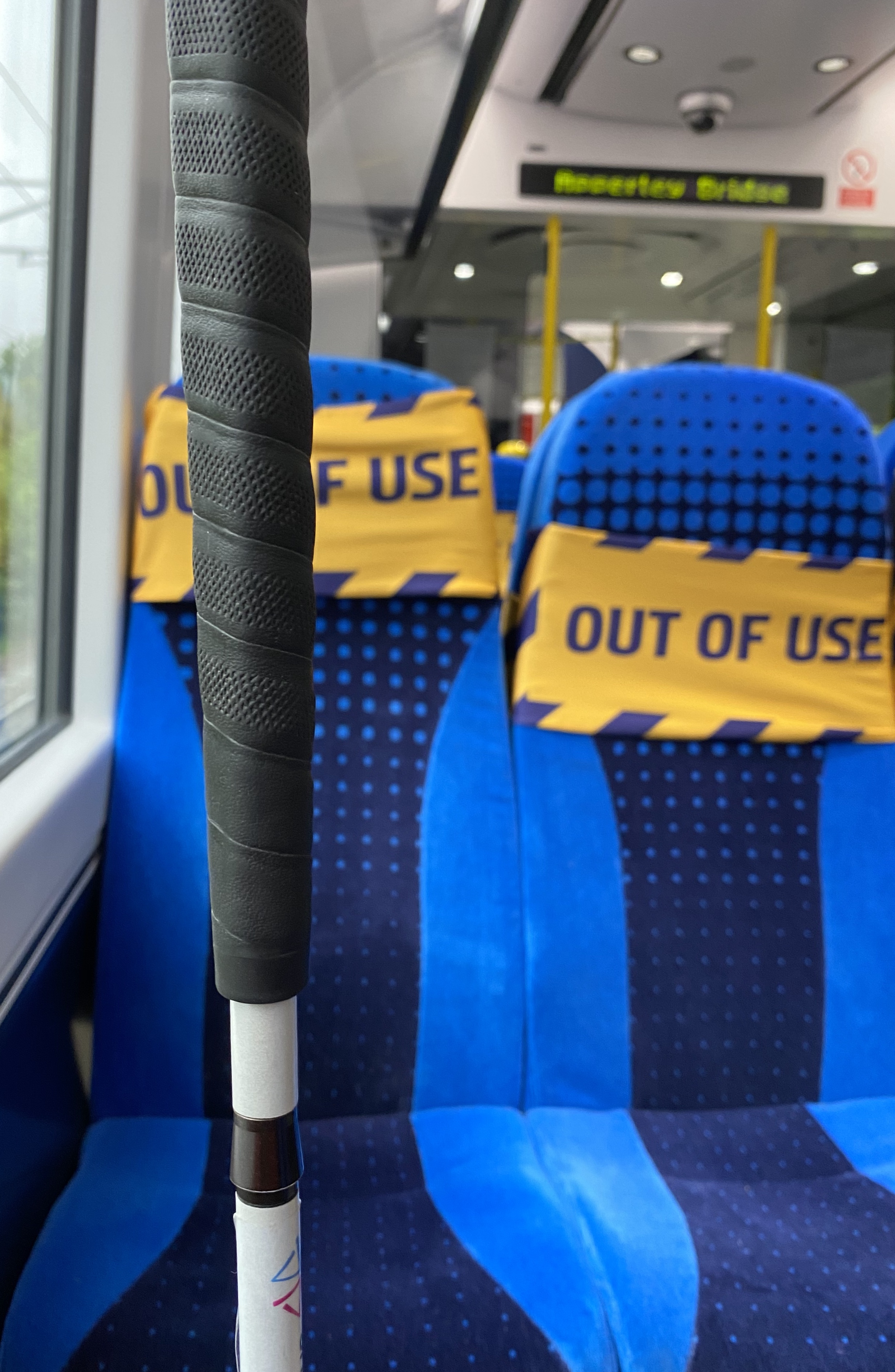 my guide cane is in the foreground, there are two blue seats the background facing me, with two 'Out Of Use' signs pace on the tops of the seat.