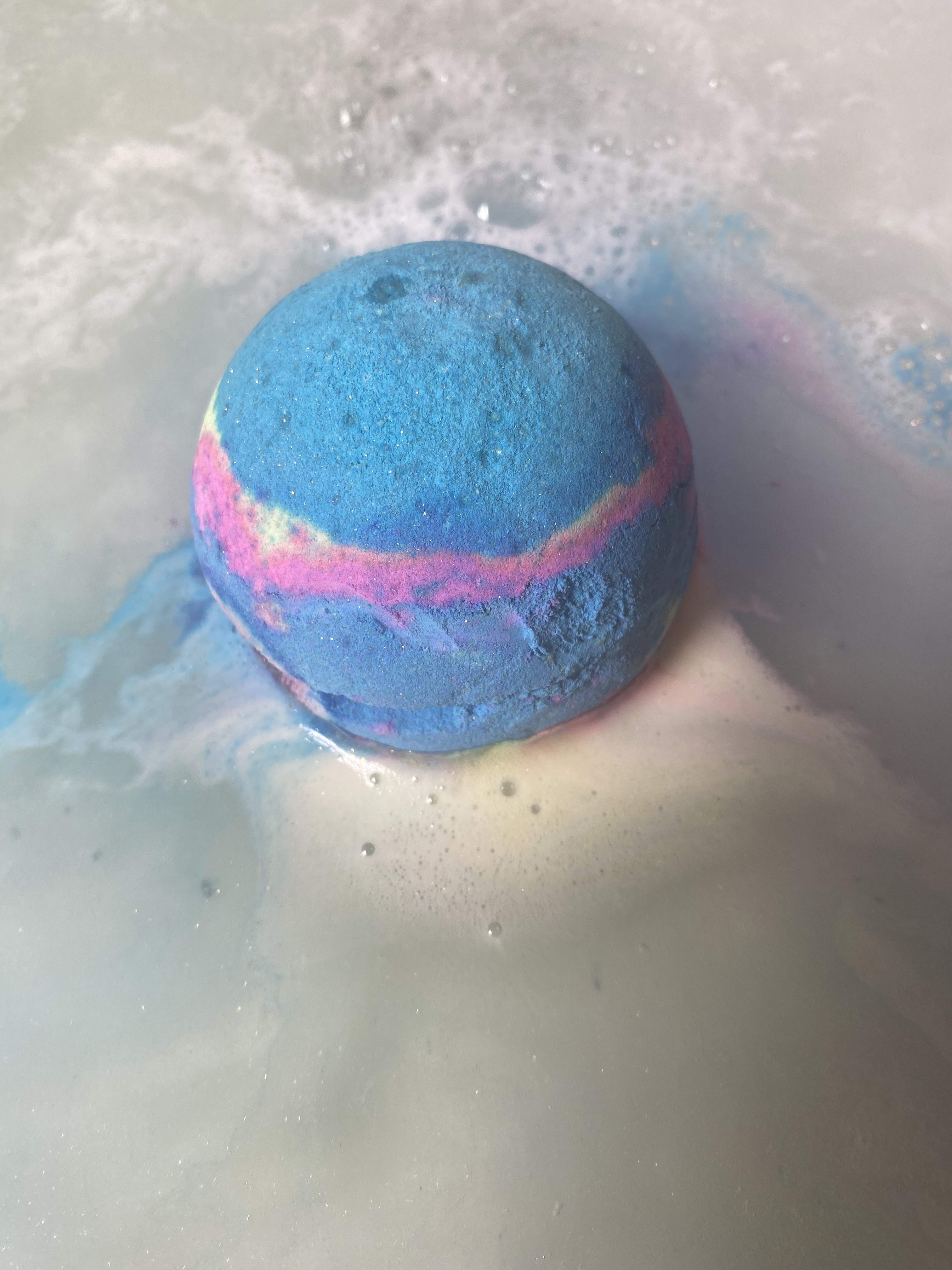 A blue bath bomb in the water, fizzing.
