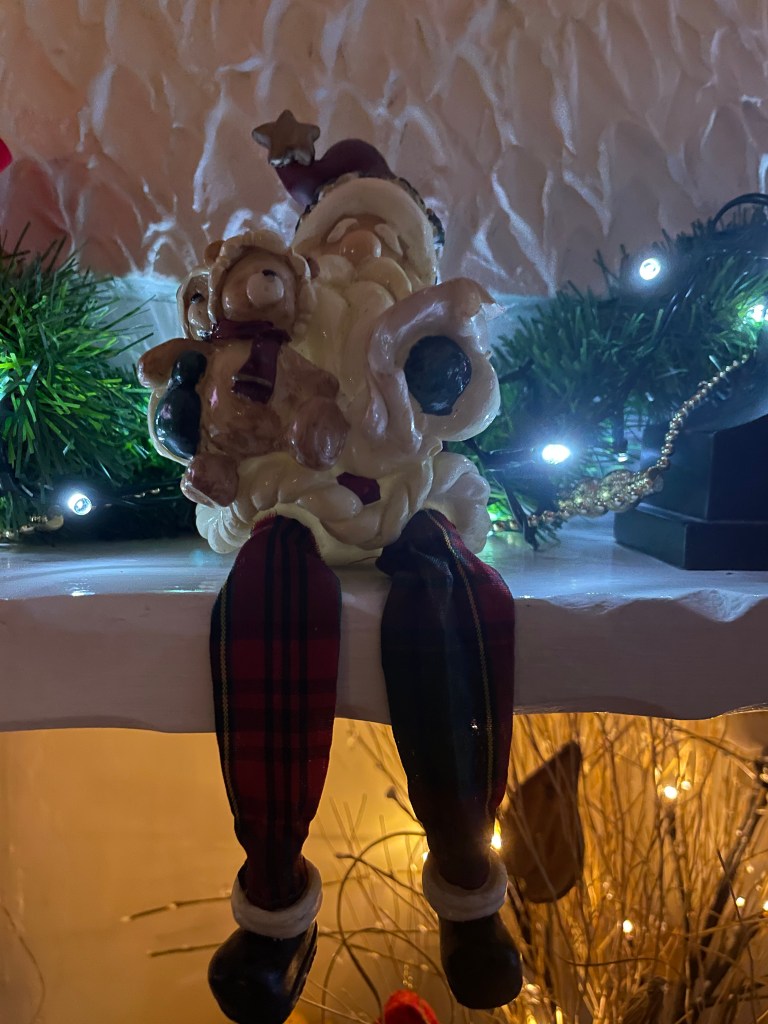 A Father Christmas is sat on the fireplace, his legs are dangling down.