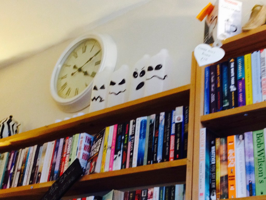 Looking at a  book shelf, there isa clock on the all above. 