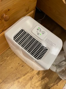 A white dehumidifier on the floor, it has a grill on the top, with three buttons on top. 