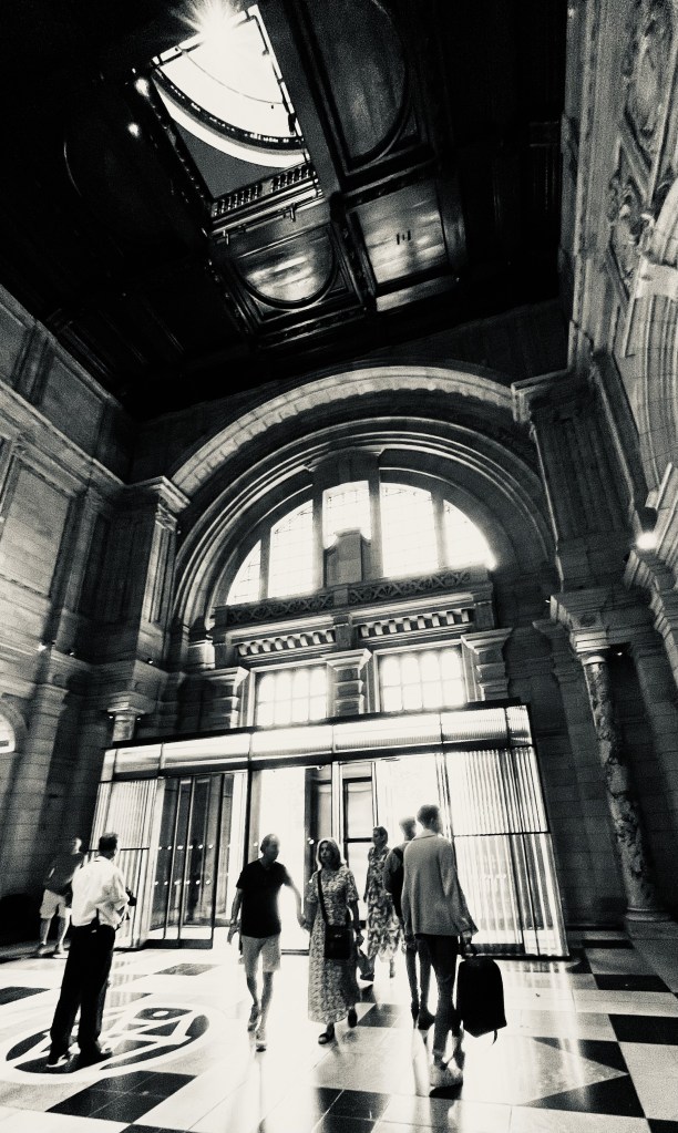 Black and White: In an atrium looking towards the door, marble floor, columns and people.