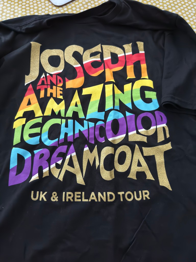 A black t-shirt with Joseph and the Amazing Technicolour Dreamcoat written across the front in rainbow colours. 