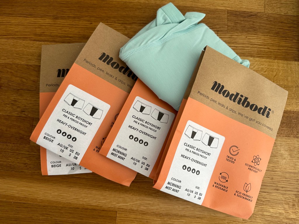 Three packets of cardboard packaging with the brand Modibodi. A pair green underwear, boys shorts style are underneath.